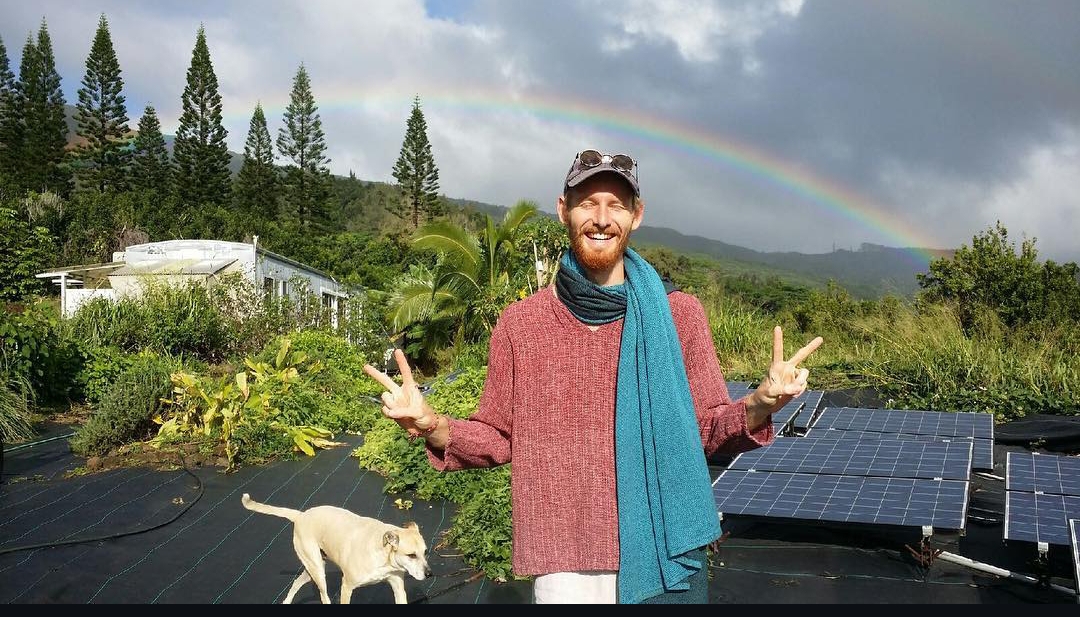Jared under a rainbow beside solar panels on a Hawaiian farm
